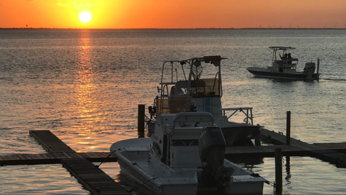 The sun sets over the Laguna Madre as a boat passes a dock on South Padre Island.